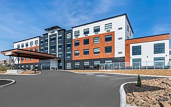 Hotel contemporáneo de cuatro niveles con revestimiento naranja, blanco y gris oscuro, y marquesina de acceso vehicular.